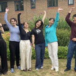 Photo of BSU interns - all standing on grass in front of building, smiling and lifting their arms up in the air.