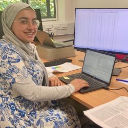 Photo of 2024 Nuffield Placement Student, Zayneb Kasur, sat at desk in front of computer screen