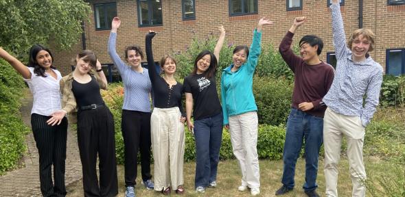Photo of BSU interns - all standing on grass in front of building, smiling and lifting their arms up in the air.